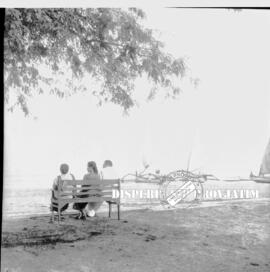 Tiga orang sedang bersantai sambil duduk dipinggir pantai pasir putih situbondo, 1956